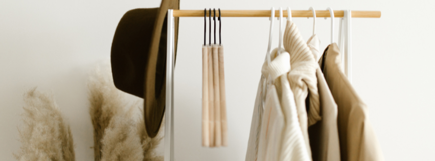 Clothing hung on a rack with a hat hung at the end of the rack